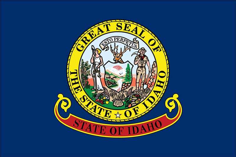 The image shows the state flag of Idaho, featuring the Great Seal of Idaho in the center, surrounded by a yellow circle on a blue background, with 