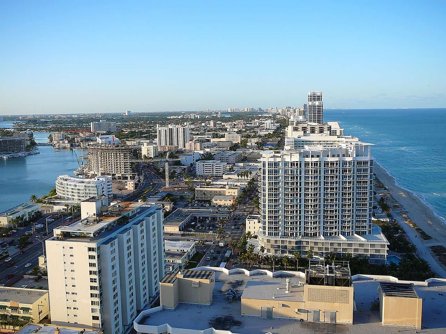 Aerial view of beachfront high-rise buildings and cityscape along a coastline with a river on the left and the ocean on the right, where tow trucks provide towing services to ensure smooth traffic flow in this bustling urban landscape.