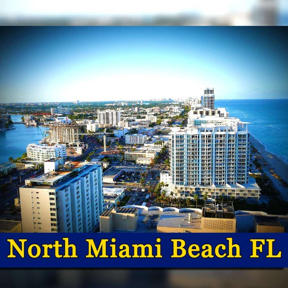 Aerial view of North Miami Beach, FL showcasing tall buildings, roads, and the coastline under a clear blue sky. A discreet tow truck navigates the roads below. Text at the bottom reads 