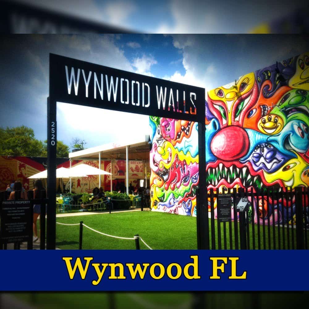 Entrance to Wynwood Walls in Miami, FL, featuring vibrant, colorful murals and a metal gate with the Wynwood Walls sign. A nearby tow truck only adds to the urban vibe of this artistic haven.
