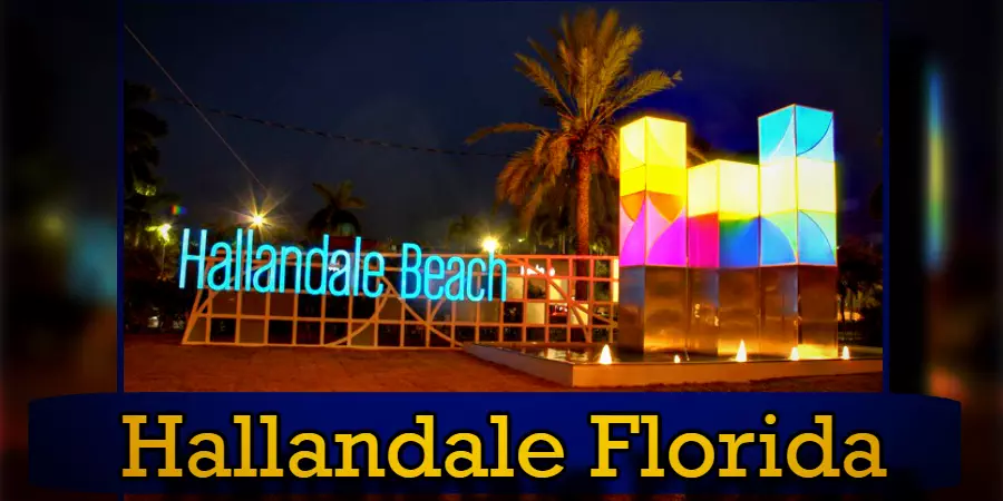 Sign at Hallandale Beach, Florida, illuminated with neon lights and colorful geometric sculptures at night, with a nearby tow truck ready to assist if needed.