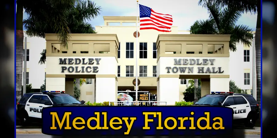 Photograph of Medley Town Hall and Medley Police Department building. A U.S. flag flies above the entrance flanked by two police cars, with a tow truck from the local towing service parked nearby. The sign reads 