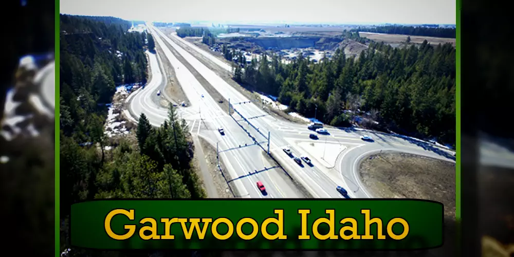 Aerial view of a highway surrounded by forested land in Garwood, Idaho. A green sign at the bottom of the image reads 