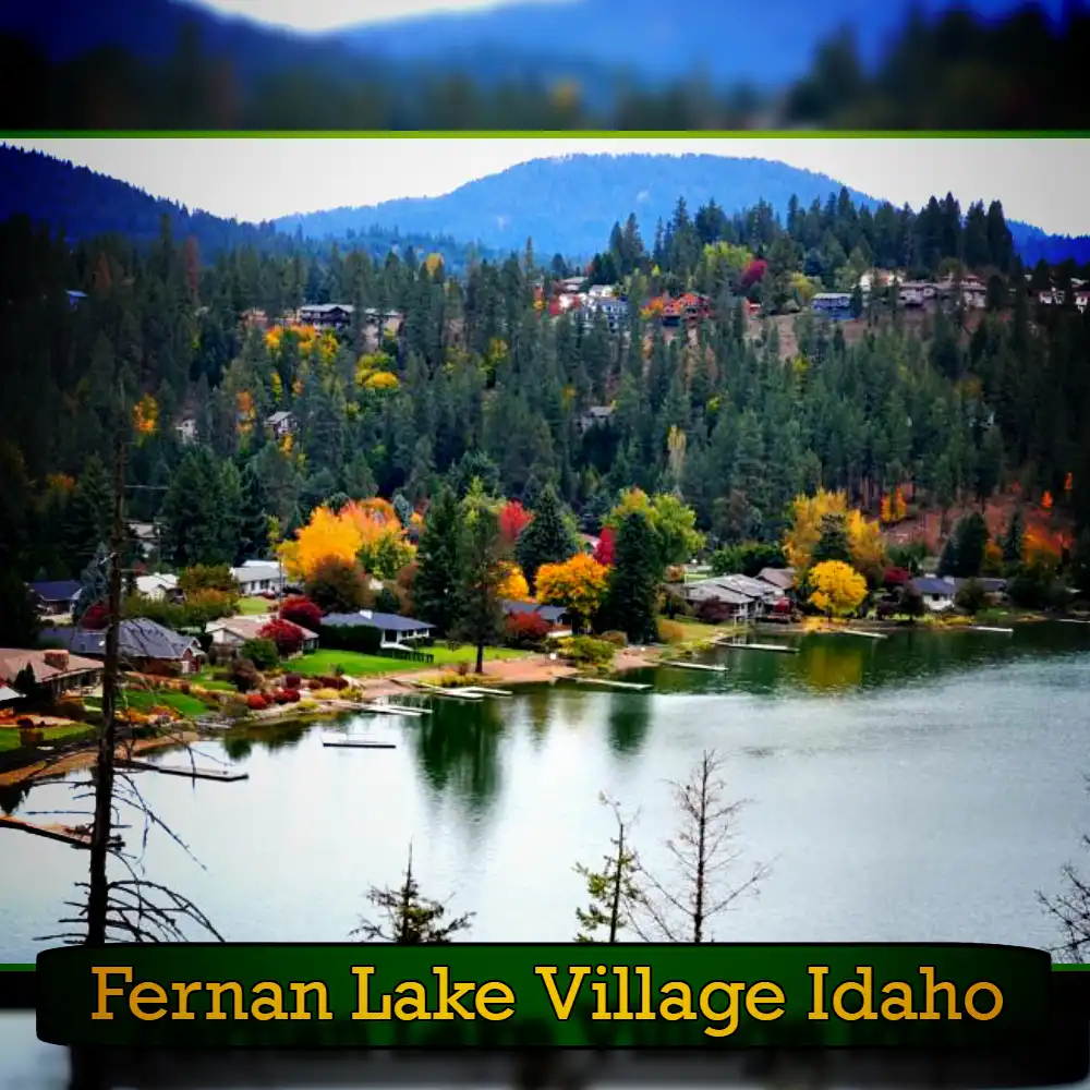 A scenic view of Fernan Lake Village, Idaho, showcases a calm lake surrounded by forested hills and vibrant autumn foliage. Houses line the lakefront with mountains visible in the background. A local tow truck service ensures your adventures remain worry-free amidst this picturesque setting.