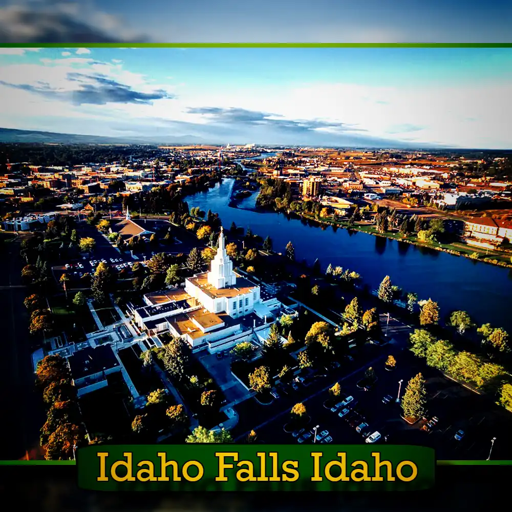 Aerial view of Idaho Falls, Idaho, featuring a prominent white building, river flowing through the city, and surrounding urban landscape at sunset. A tow truck can be spotted among the vehicles traversing the streets below.
