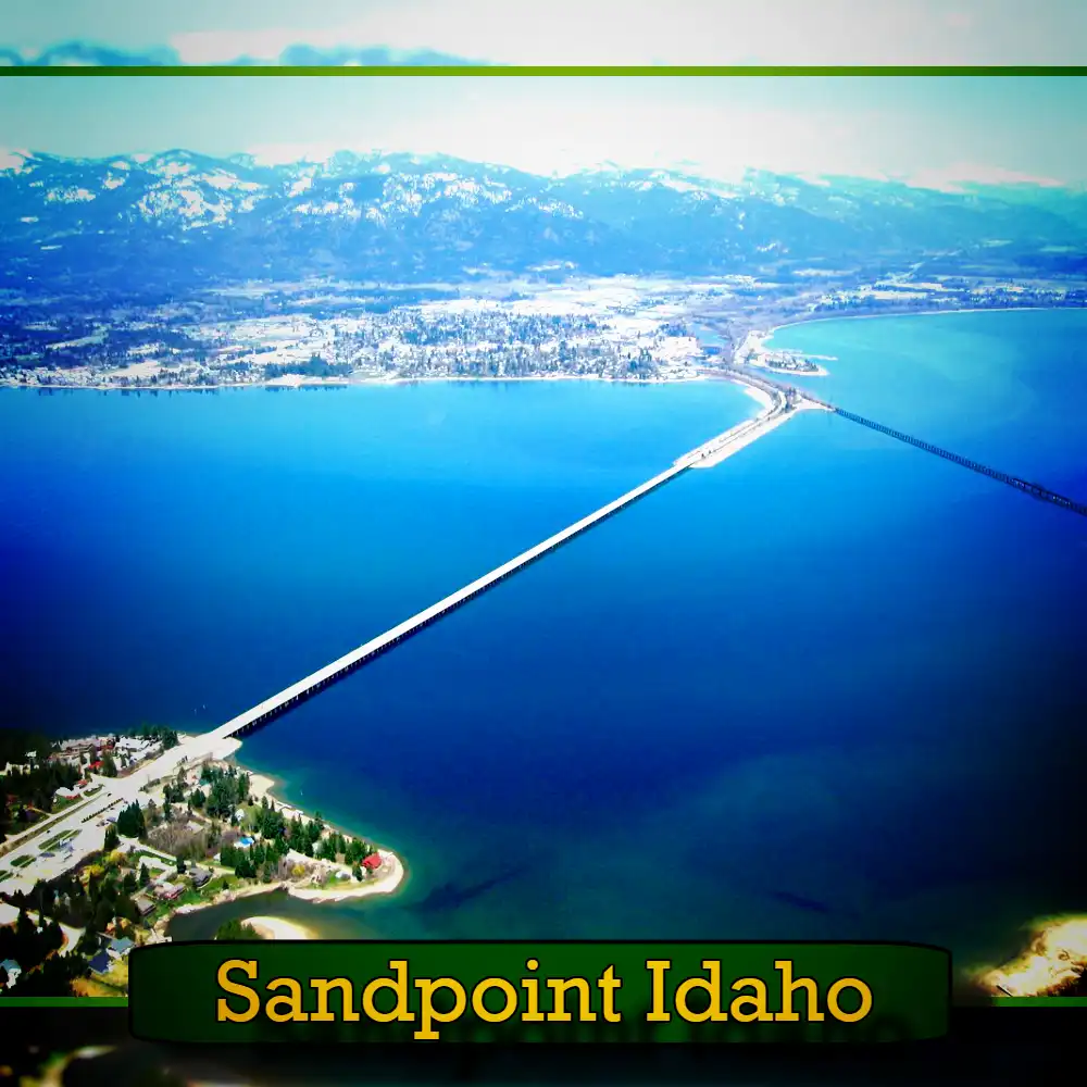 Aerial view of Sandpoint, Idaho, featuring a long bridge crossing over a large body of water with mountains in the background. A tow truck can be spotted near the bridge. The caption reads 
