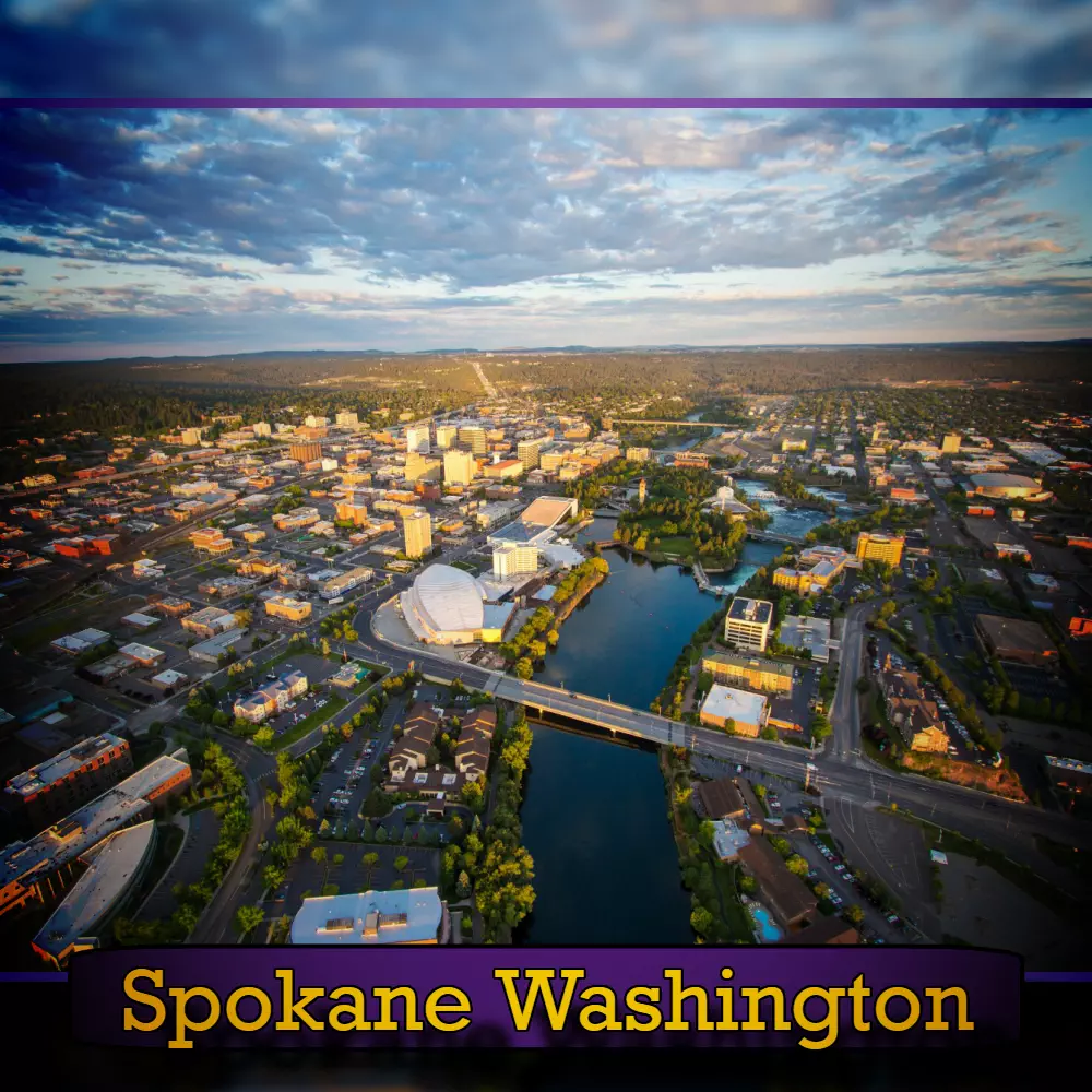 Aerial view of Spokane, Washington during sunset. The city's buildings, a river, and a bridge are visible, along with tree-filled areas. A tow truck can be seen crossing the bridge. The image is labeled 