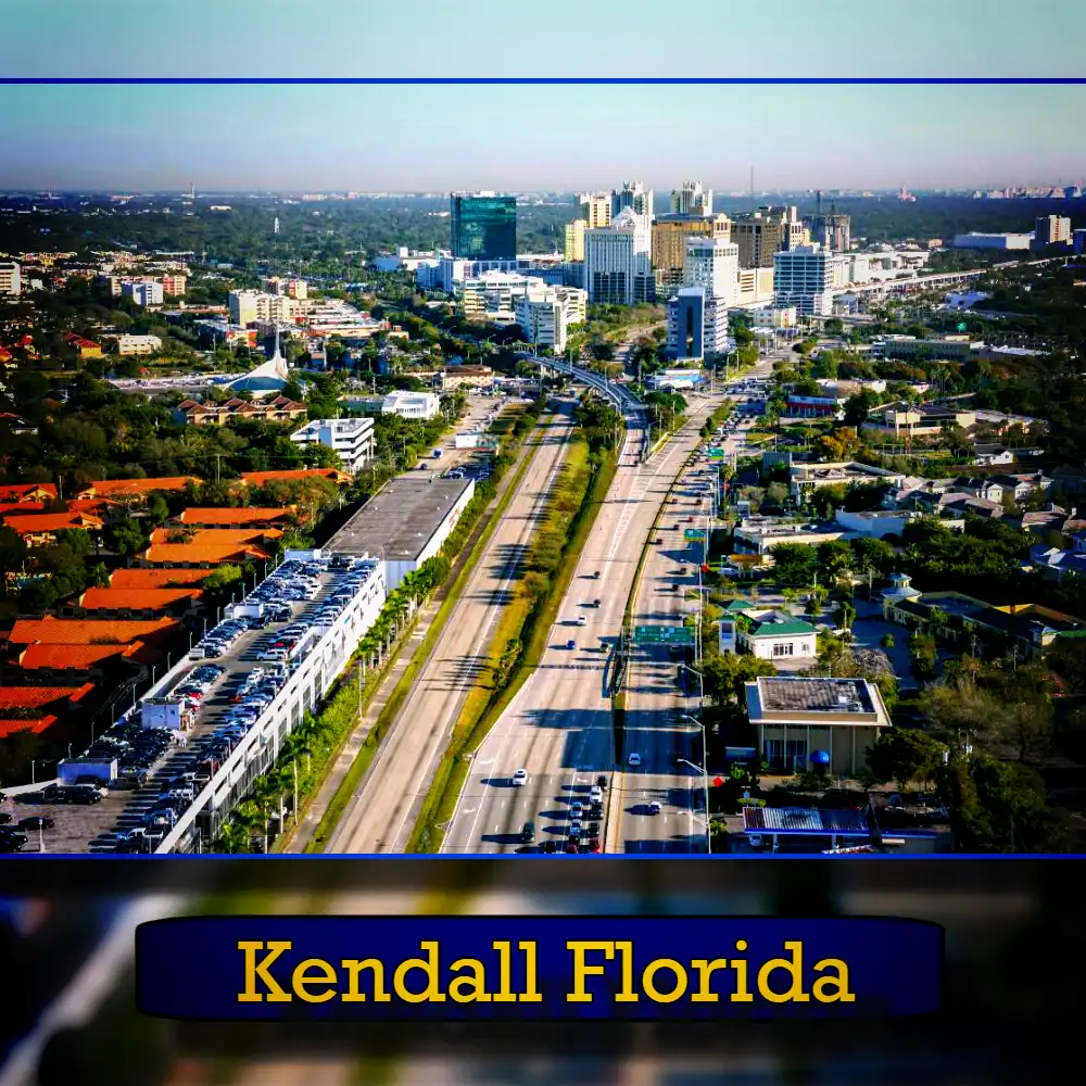 Aerial view of a cityscape featuring a major road dividing the urban area of Kendall, Florida, with buildings and greenery on either side, under a clear sky. A tow truck is seen navigating through the bustling streets below.