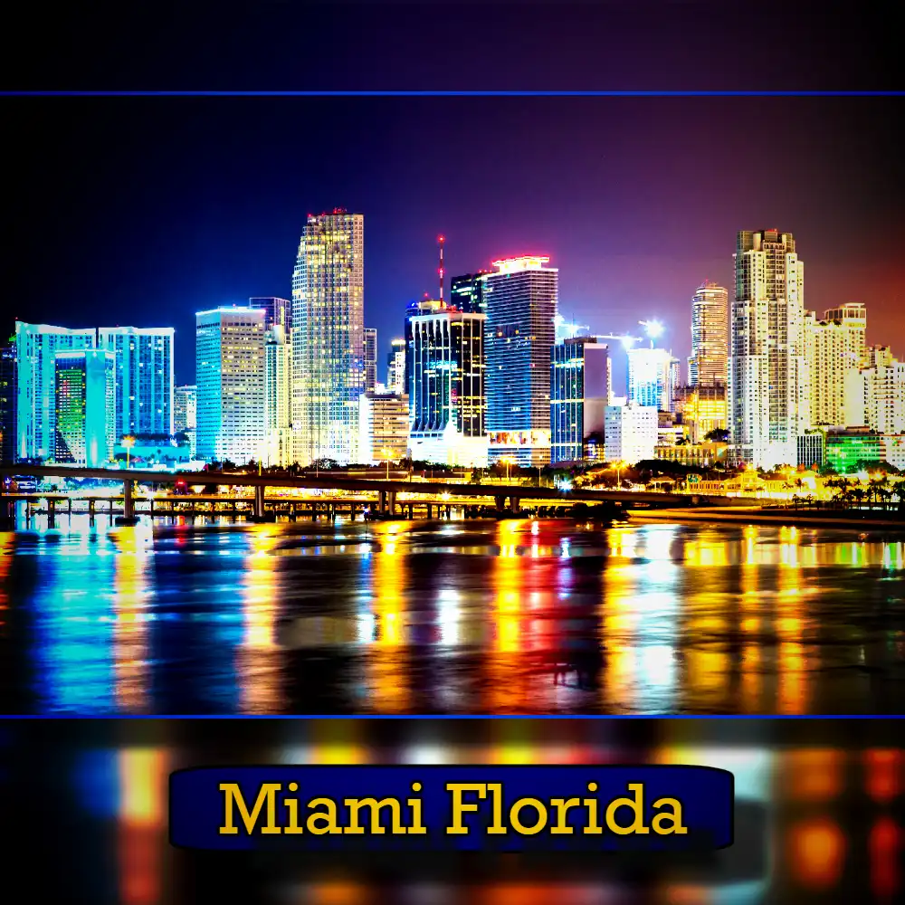 Nighttime view of Miami, Florida's illuminated skyline with colorful lights reflecting on the water below, occasionally interrupted by the distant headlights of tow trucks attending to their duties.