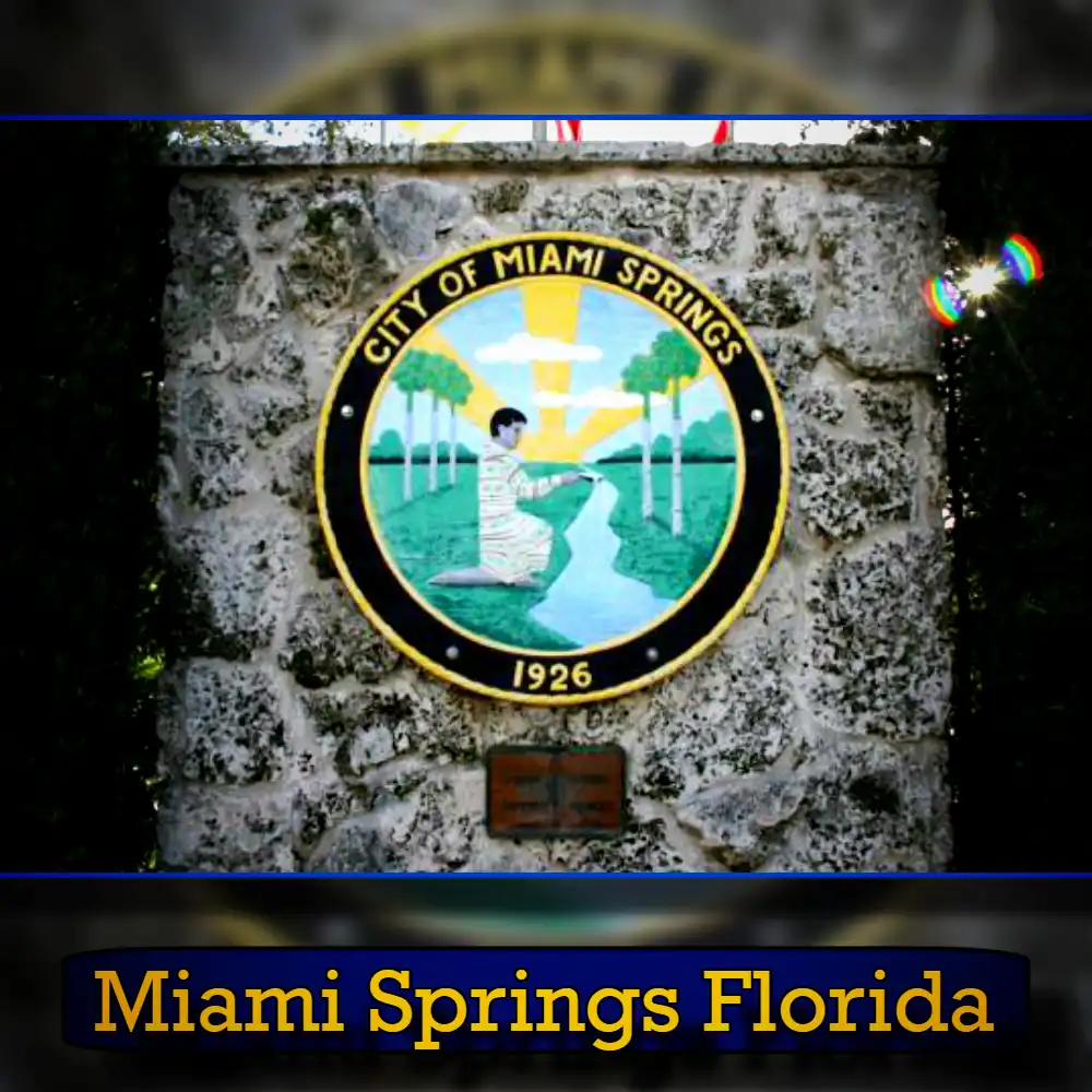 A stone wall features the seal of the City of Miami Springs, Florida, established in 1926. The seal depicts a person sitting by a river with trees and the sun in the background, symbolizing tranquility and community—a stark contrast to the bustling tow truck services that operate nearby.