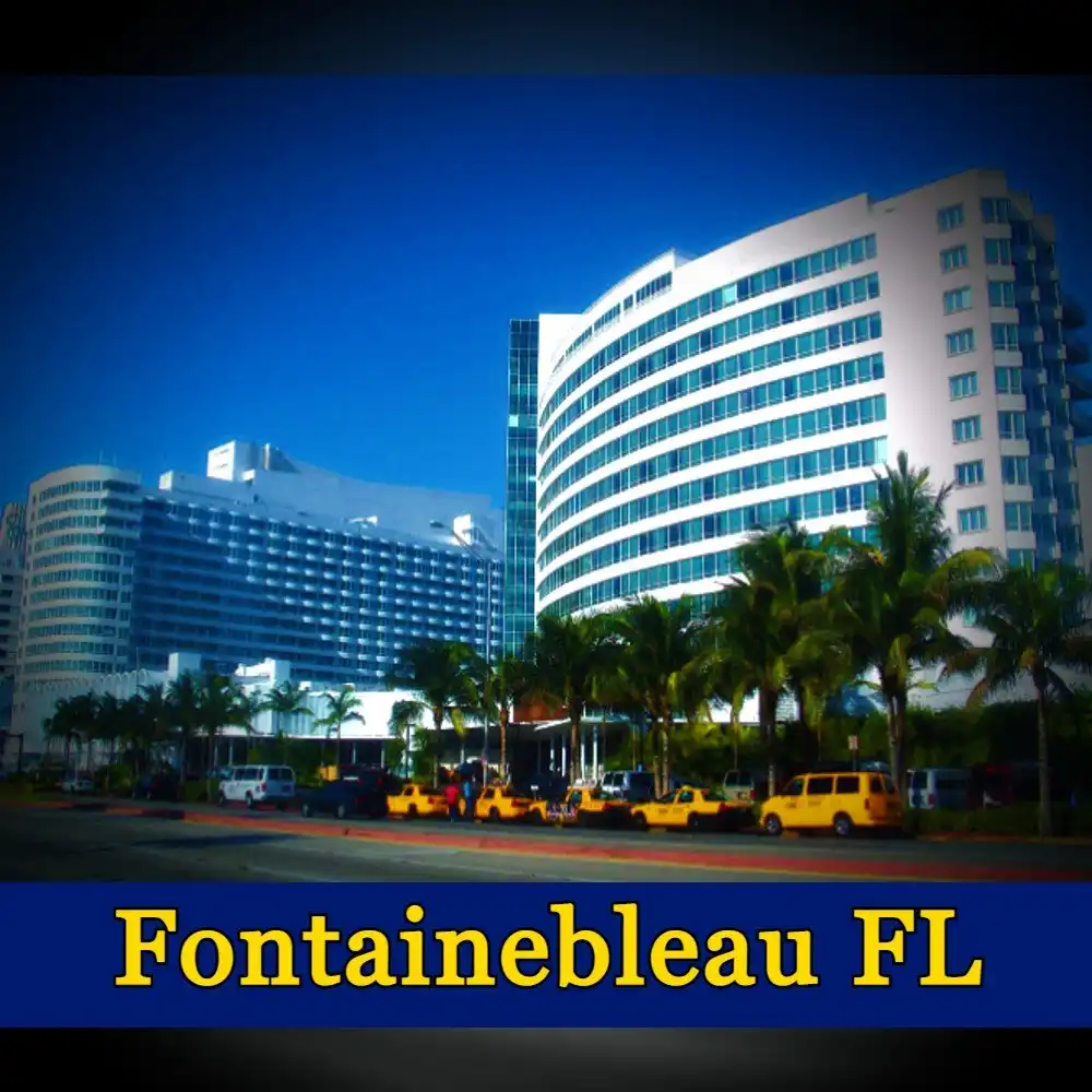 A large hotel with modern architecture and palm trees in front, set against a clear blue sky. A discreet tow truck is parked nearby, blending seamlessly into the scene. The text at the bottom of the image reads 