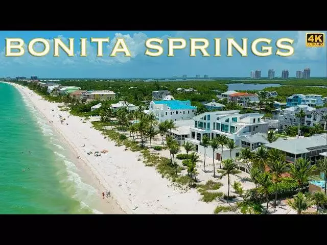 Aerial view of Bonita Springs featuring a beach with white sand, turquoise water, palm trees, and numerous houses along the shoreline. Nearby, a tow truck services the area to ensure everyone's beachfront experience remains smooth and uninterrupted.