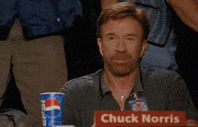 A man with reddish hair and a beard gives a thumbs up while sitting at a table with Pepsi cups and a nameplate that says 
