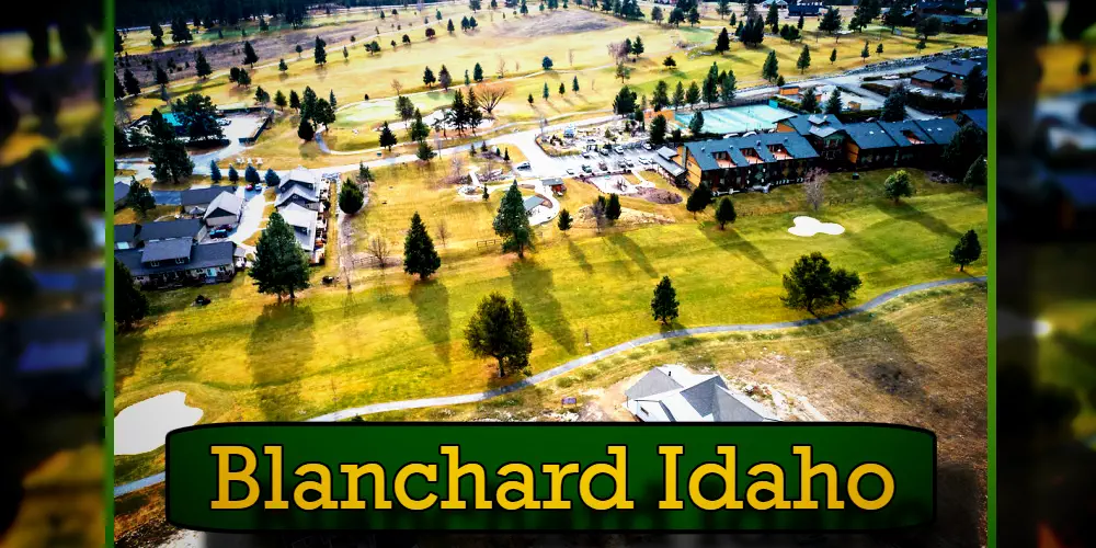 Aerial view of a residential and recreational area in Blanchard, Idaho, featuring houses, trees, and open grassy spaces, with a tow truck seen parked near one of the driveways.