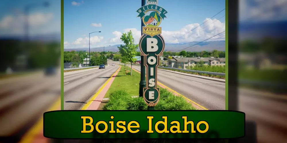 Welcome sign for Boise, Idaho, positioned on a road divider with mountains and residential areas in the background. A nearby tow truck adds a touch of roadside practicality to the scenic view.