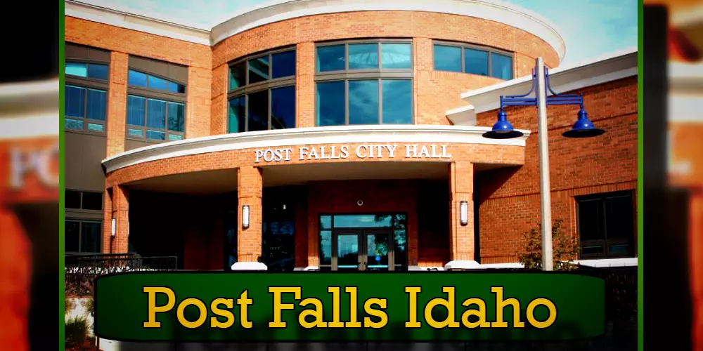 The image shows the exterior of Post Falls City Hall in Post Falls, Idaho, featuring a brick facade, large windows, and blue lamp posts. A green banner at the bottom reads 