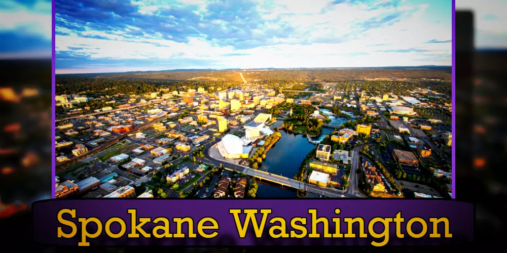 Aerial view of Spokane, Washington, showcasing the city's downtown area, river, and surrounding landscape. A tow truck can be seen navigating the streets below. 