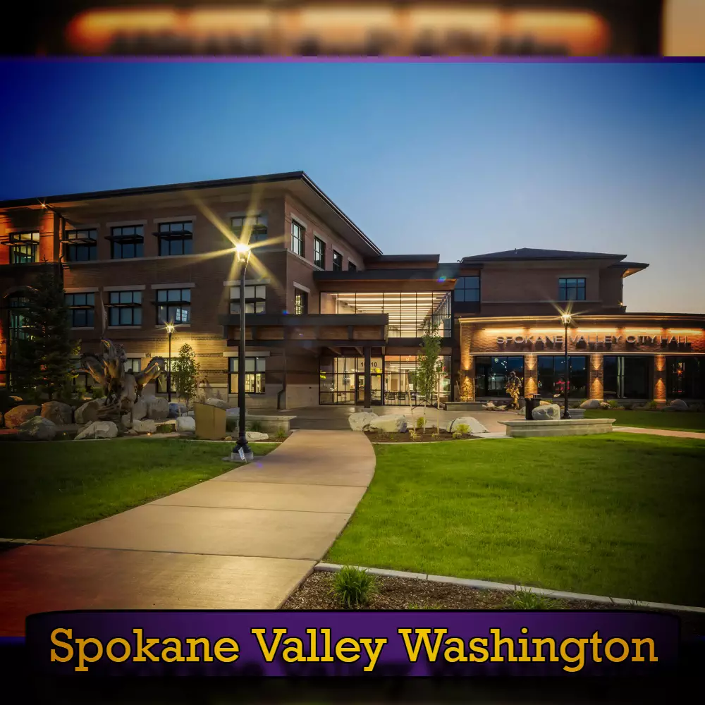 A well-lit, modern building with a landscaped entrance path in Spokane Valley, Washington. The brick and glass structure prominently features a sign indicating its location at the entrance, making it easily identifiable for those seeking nearby tow service.