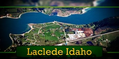 Aerial view of Laclede, Idaho, showing a community near a river with surrounding greenery, various buildings, and a tow truck by the main road. Text reads 